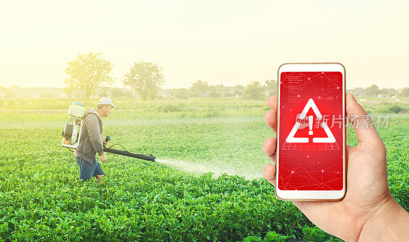 手机在手，显示一个警告的背景，一个农民与雾喷雾器在农场上。使用危险化学品处理植物和农作物。潜在的健康危害。