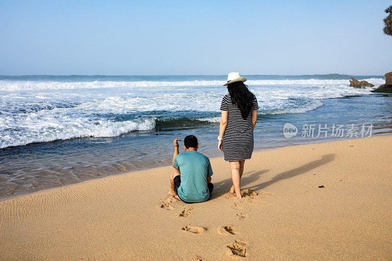 一对亚洲年轻夫妇坐在海滩上遥望远方