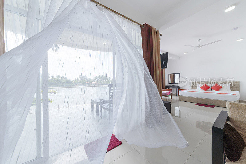 现代空旷的酒店房间里，风吹动了敞开的阳台窗户上的窗帘。