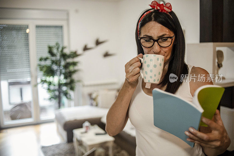 一位戴着眼镜的黑发老妇人正在她温暖的家中休息和散步，一边看书一边看书。一位年轻的老妇人一边看书一边拿着一杯茶走进她的公寓