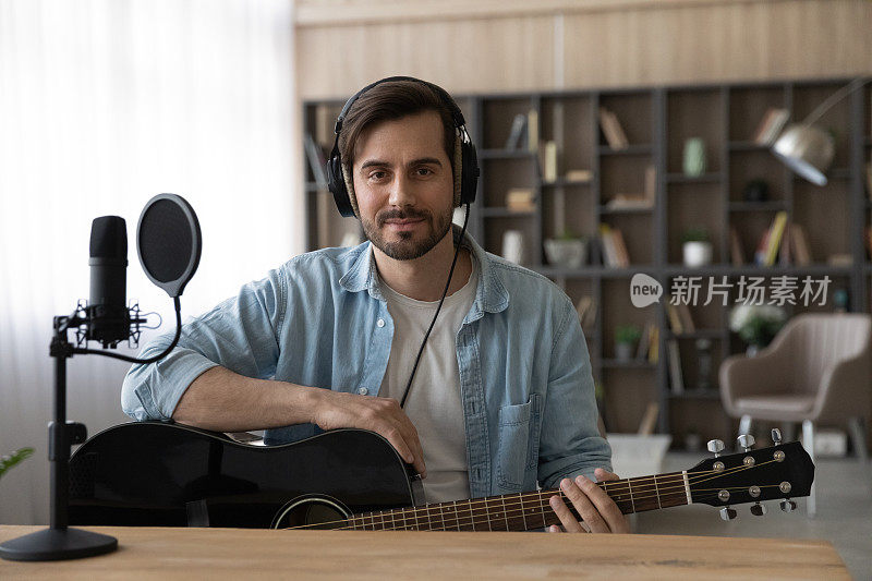 肖像男子戴着耳机拿着吉他，坐在家庭工作室