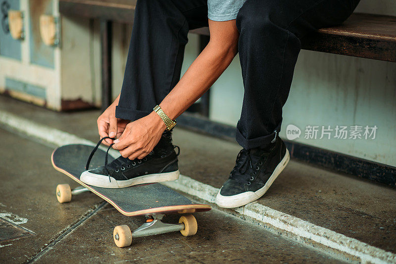 亚洲男性滑板手系鞋带在一个滑板公园