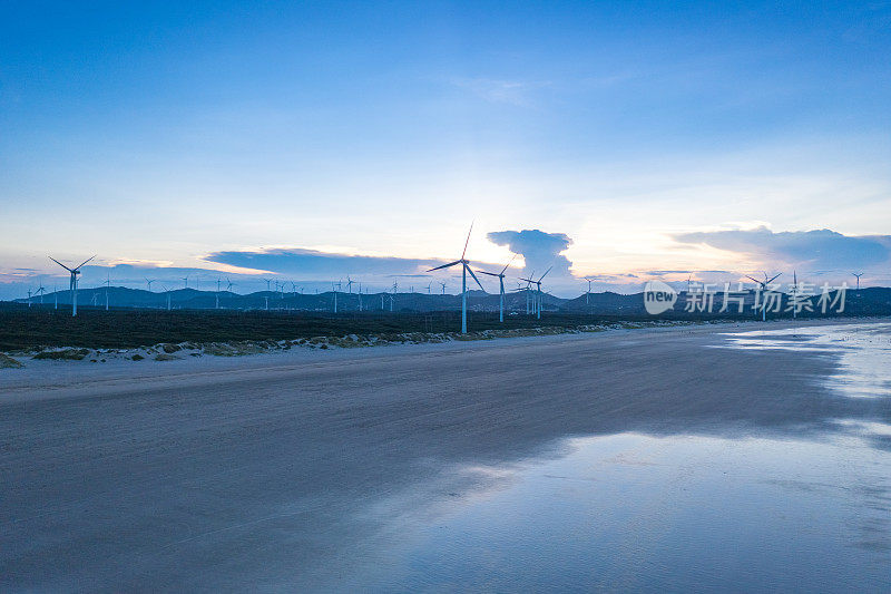 黄昏时分，海滩上的一排风力涡轮机