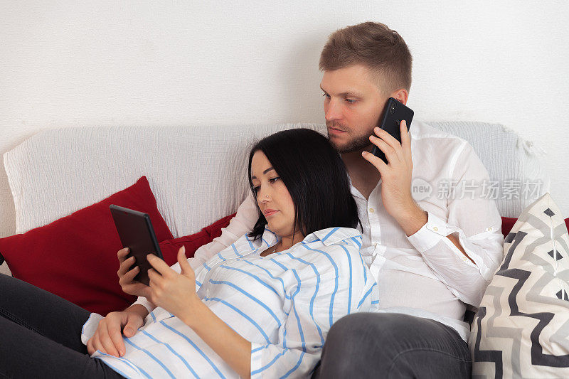 男人抱着女人在沙发上打电话，女人躺着看平板电脑