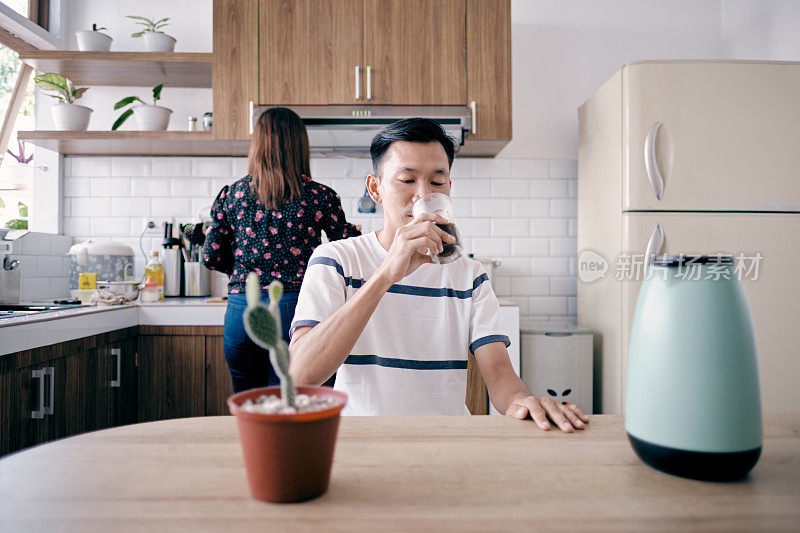 一个年轻人在喝咖啡，而他的妻子在准备早餐