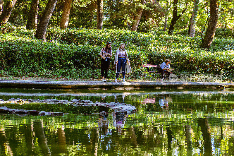 好奇的女性朋友们在城市休息时，欣赏着公园里美丽的池塘