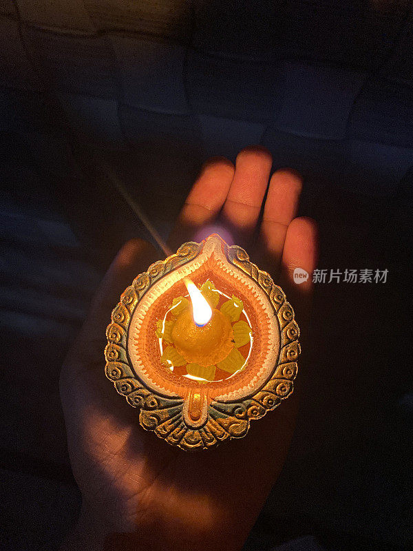 一个不认识的人手拿着一个点燃的，充满油的粘土diya的图像，排灯节油灯与点燃的灯芯，闪烁的火焰在黑暗中，排灯节庆祝，上升的观点