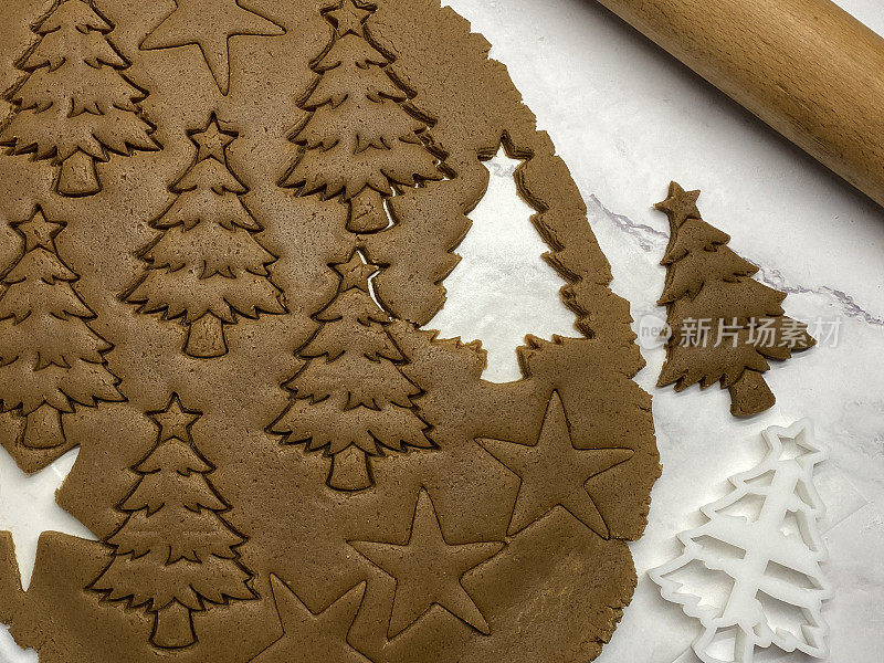 自制的姜饼曲奇面团用塑料圣诞树饼干刀和擀面棍在防油羊皮纸上铺开，树形和星形切出形状，家庭烘焙，高架视野
