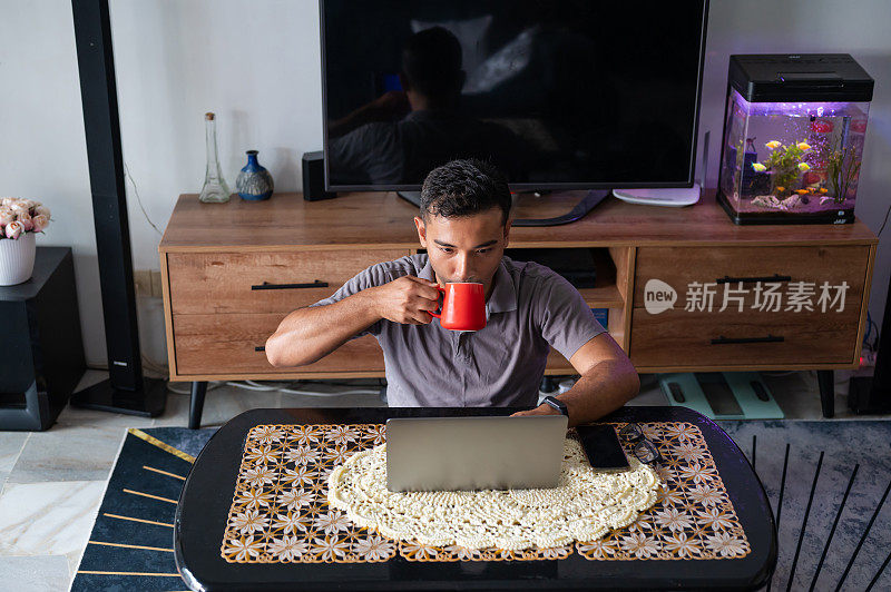 亚洲穆斯林男人喝着咖啡，在客厅里工作。