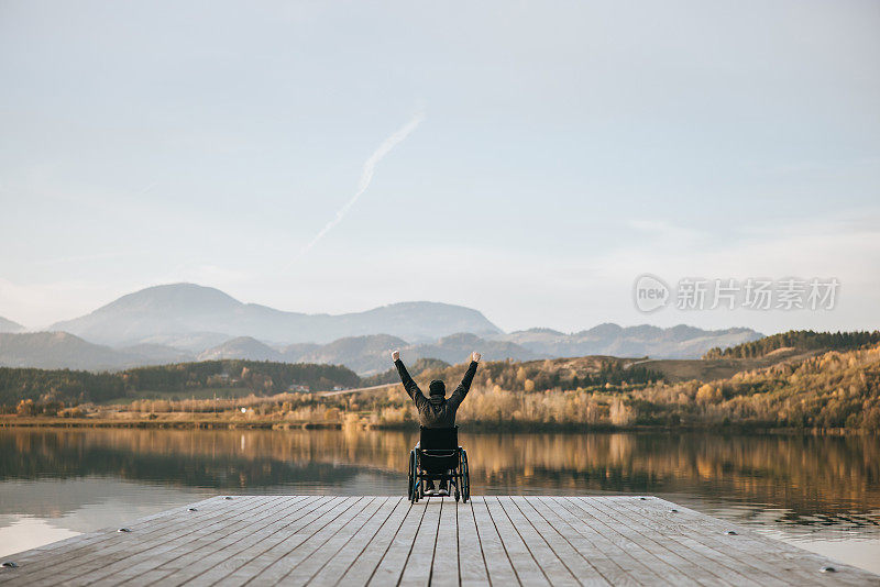 残疾人在轮椅上举起手臂，在码头欣赏大自然