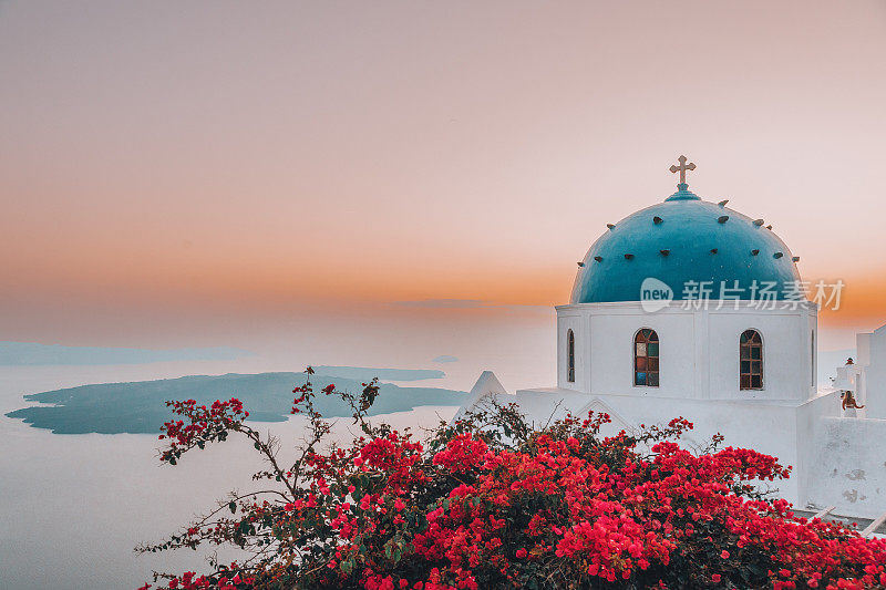 希腊圣托里尼岛上著名的传统蓝色圆顶教堂和红色花朵