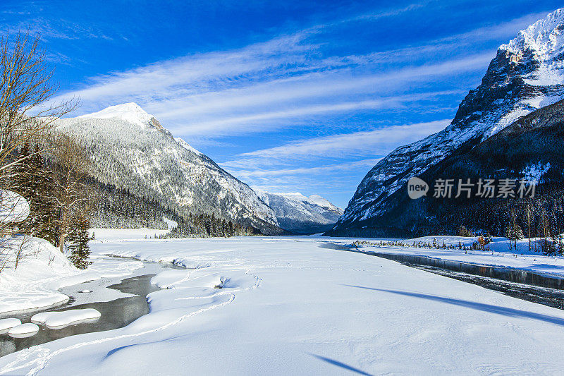 田园诗般的冬季场景，明亮的蓝色天空与积雪覆盖的河流和山脉景观背景。