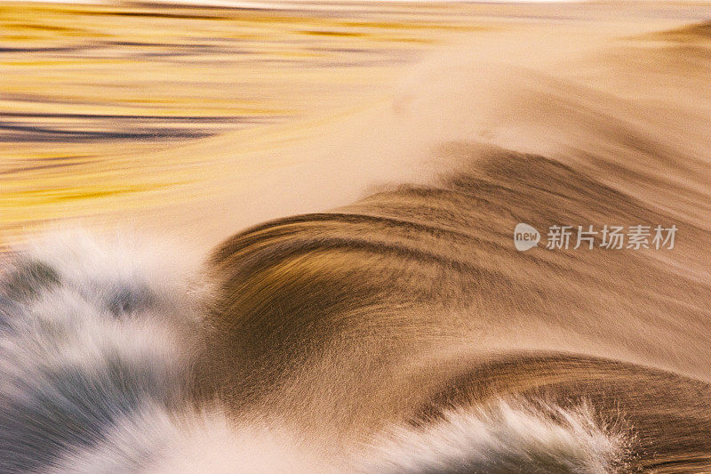 日落时分，海滩上的海浪倒映着明亮的天空