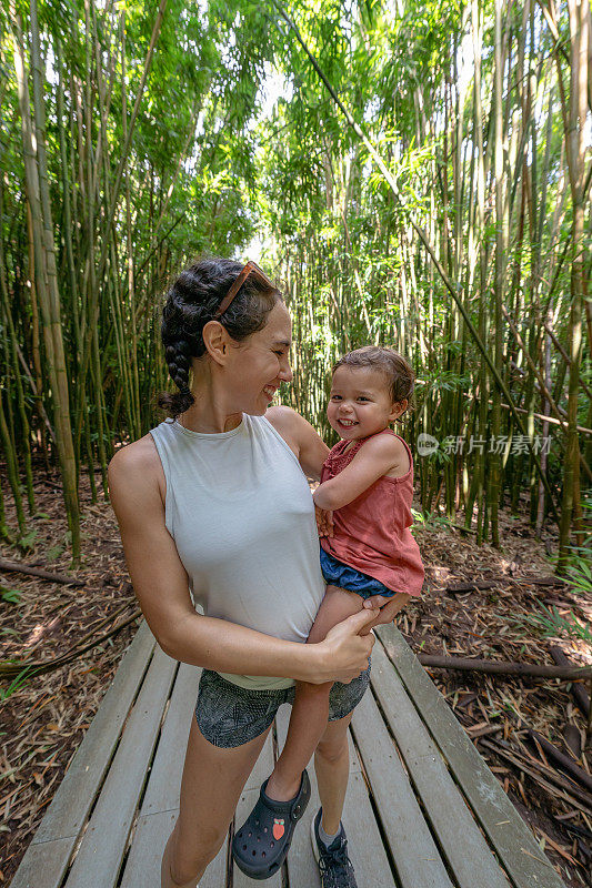 妈妈抱着蹒跚学步的女儿在热带森林徒步旅行