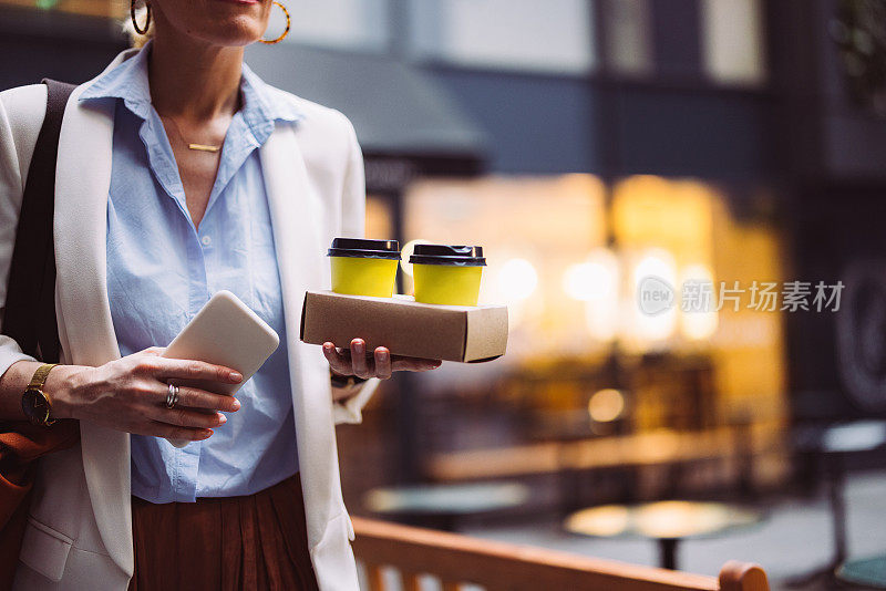 特写照片的女人手拿两杯咖啡和智能手机在户外