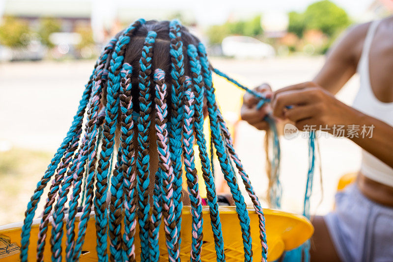 一个穿着西装的女孩在一个阳光明媚的日子里在她的头发上编着非洲辫子