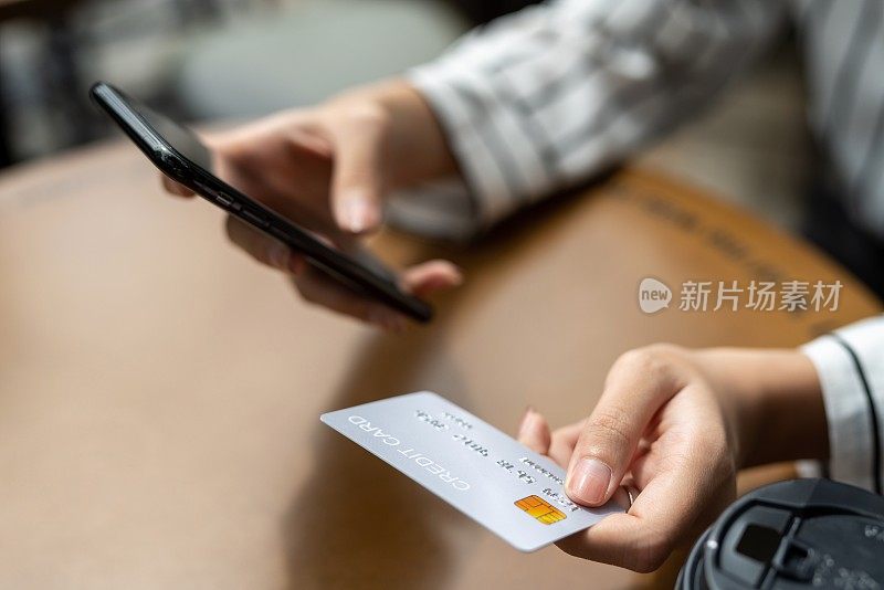 年轻聪明的亚洲女商人通过她的智能手机使用她的信用卡在一个随机的咖啡馆进行在线支付