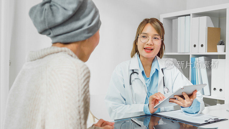 年轻的亚洲女医生在健康诊所用平板电脑为患有癌症的女病人进行会诊时的医疗结果。医疗保健。
