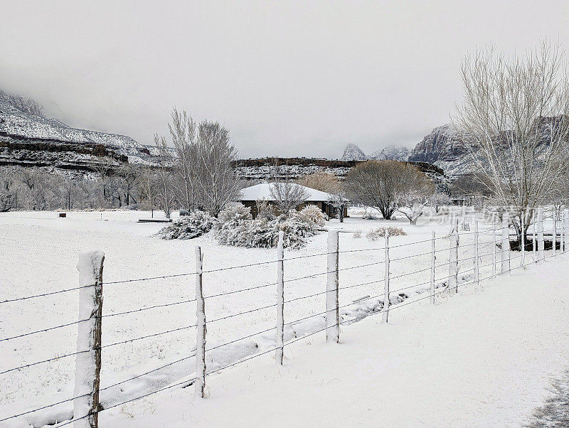 在犹他州洛克维尔，一场大雪过后，格拉夫顿路上的牧场房屋和灌溉沟渠，背景是锡安国家公园