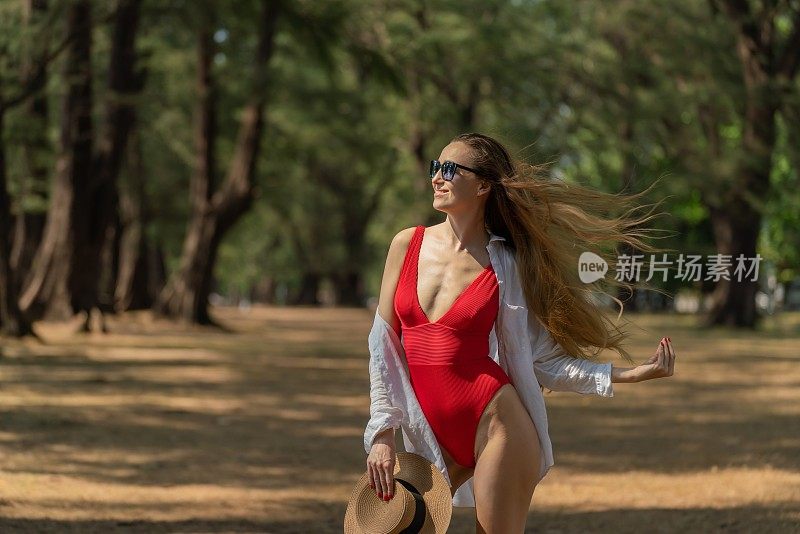 美丽的白人女性性感的女人在红色泳装比基尼寒冷和放松的帽子在她的头上快乐地微笑在森林的海滩