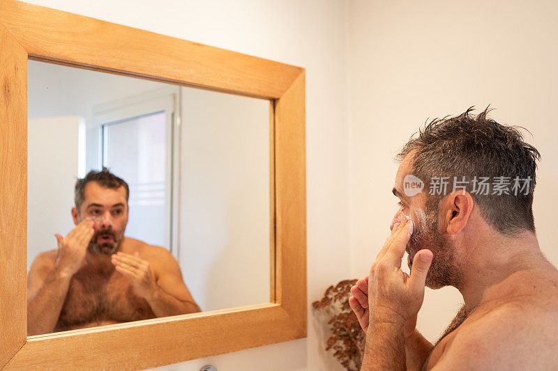 一个成年男子在镜子前往脸上抹面霜
