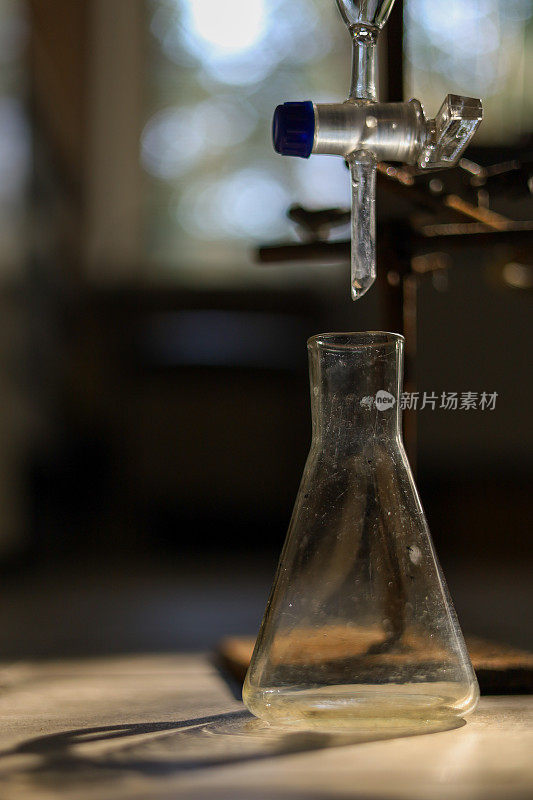 在一个废弃的化学实验室里，一个又旧又脏的空玻璃烧瓶，放在分隔漏斗下面