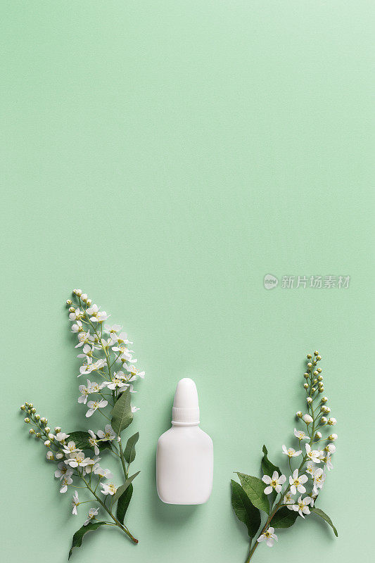 季节性的春季过敏，春天的树枝树上有白色的花朵和绿色背景上的模拟鼻喷雾剂瓶，过敏的概念开花。抗组胺喷雾剂用于鼻塞