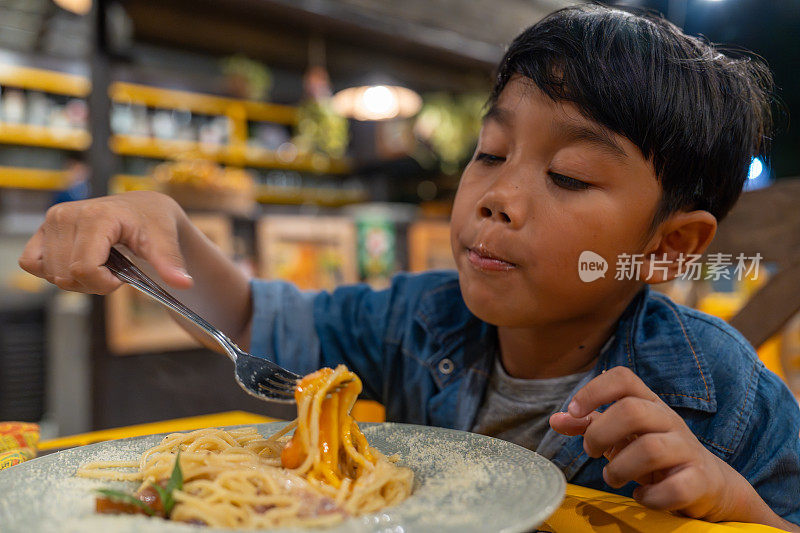 老挝琅勃拉邦，一个亚洲小男孩晚上在餐馆里吃意大利面。