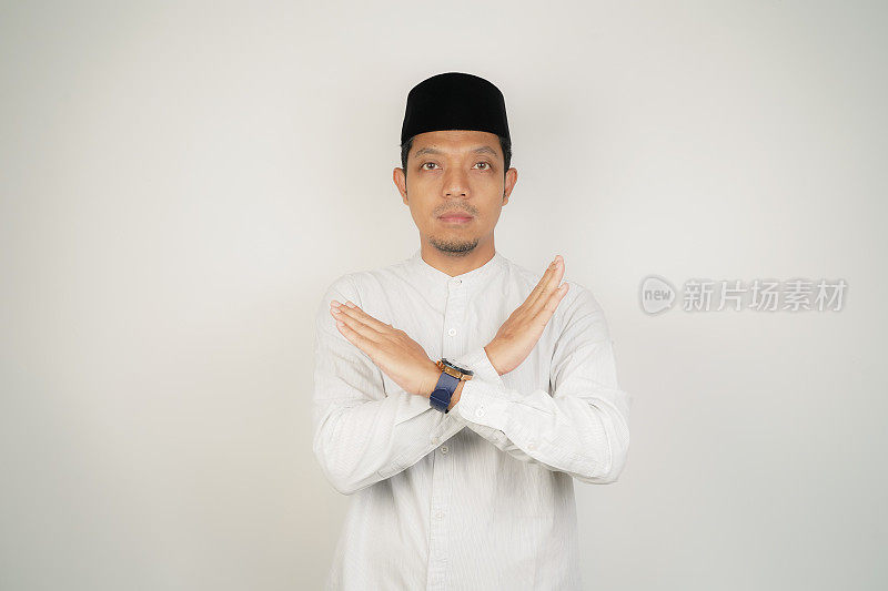 亚洲穆斯林男子表现出“停止”或“拒绝”的表情，双臂交叉做否定的手势，孤立的背景。