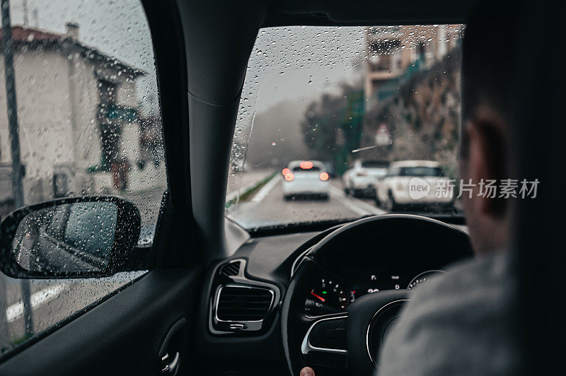 一名男子在暴雨中驾驶汽车在城市街道的后视图肖像。