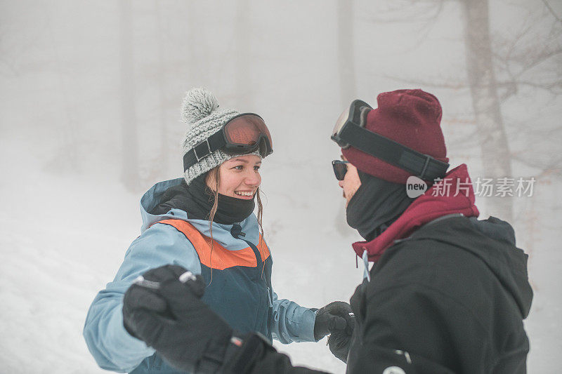 在山上滑雪时，一个女人微笑着看着她的男朋友