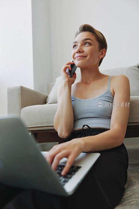一个拥有笔记本电脑和手机的自由职业女性，穿着家常的衣服，剪着短发，坐在地板上工作，有自由的复印空间