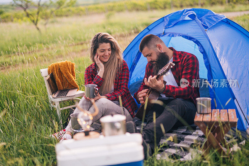 一对年轻夫妇在大自然中露营，一个男人在弹吉他，他们在一起玩得很开心
