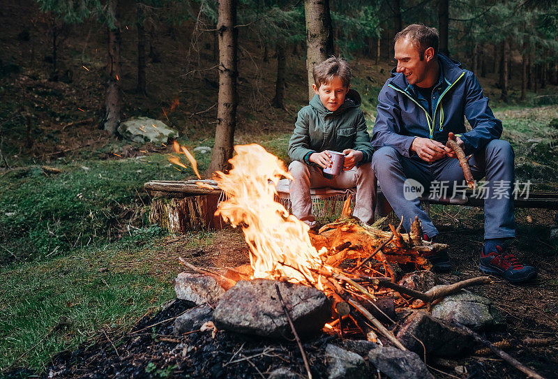 父亲和儿子在篝火旁取暖，喝茶聊天