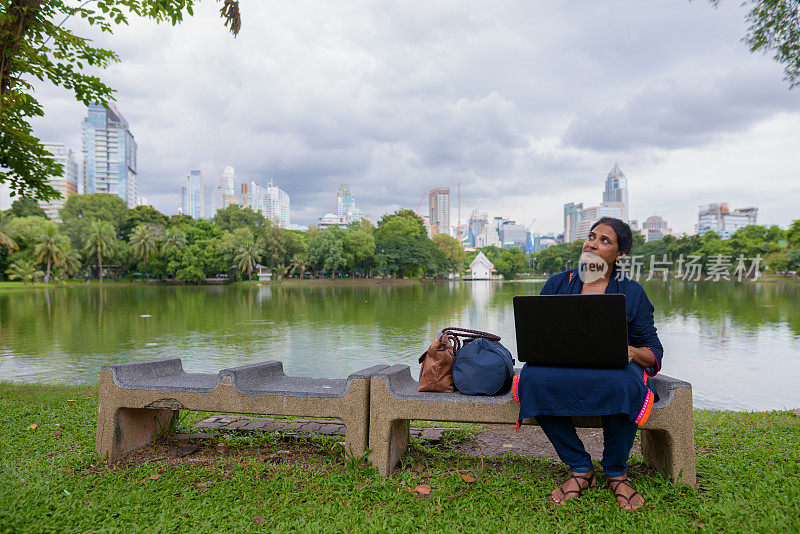 成熟美丽的印度女商人的肖像放松在曼谷的城市的公共公园
