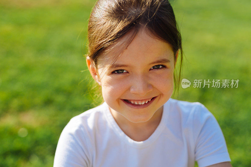 一个微笑的小女孩的肖像在草地的背景