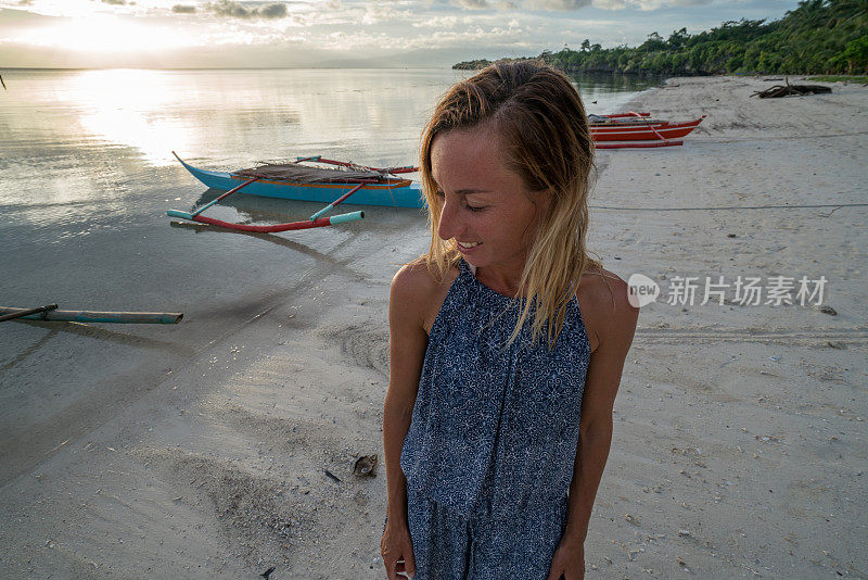 日落时分，一个年轻女子走在热带海滩上，凝视着大自然