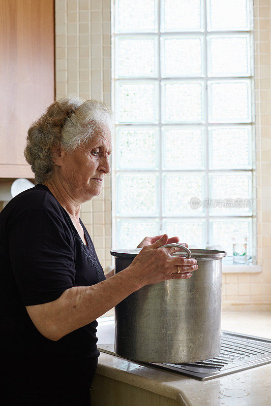 一位老妇人在厨房里拿着一个巨大的锅子准备食物