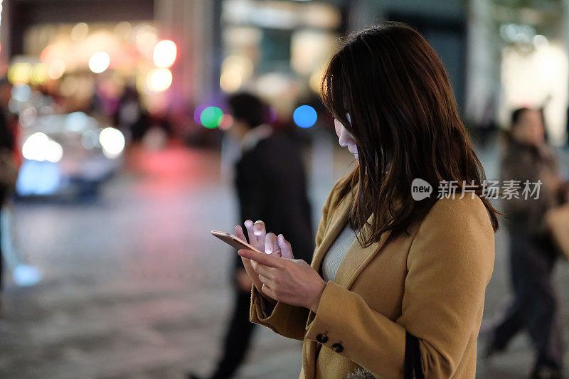 女人看智能手机在街上的照明