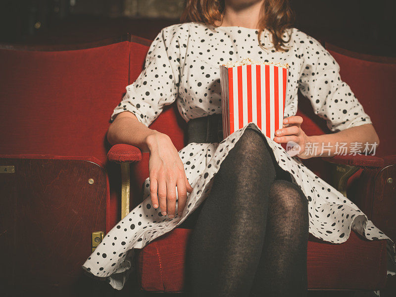 年轻女子坐在电影院吃爆米花