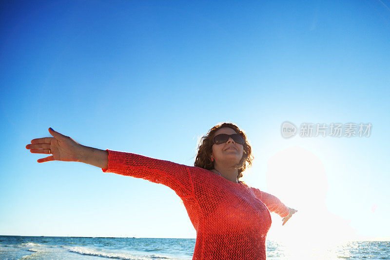 女人在海边张开双臂迎接日出