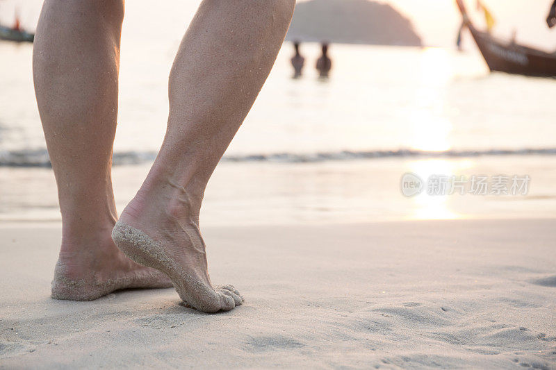 女人的双脚横越白沙滩，日出