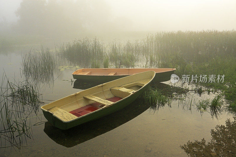 清晨的阳光照在停泊在雾蒙蒙的湖面上的两只木船上