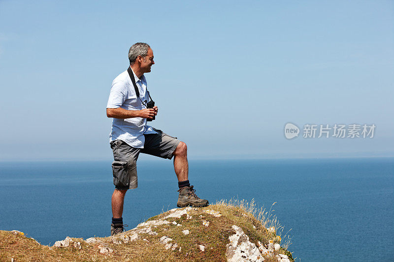 一个成熟的白种人拿着望远镜站在悬崖顶上