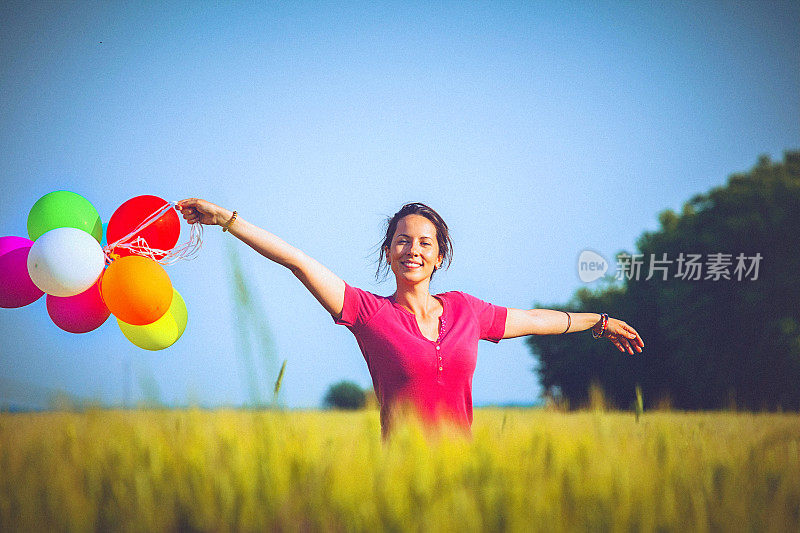 兴高采烈的女人拿着彩色的气球，跑过麦田