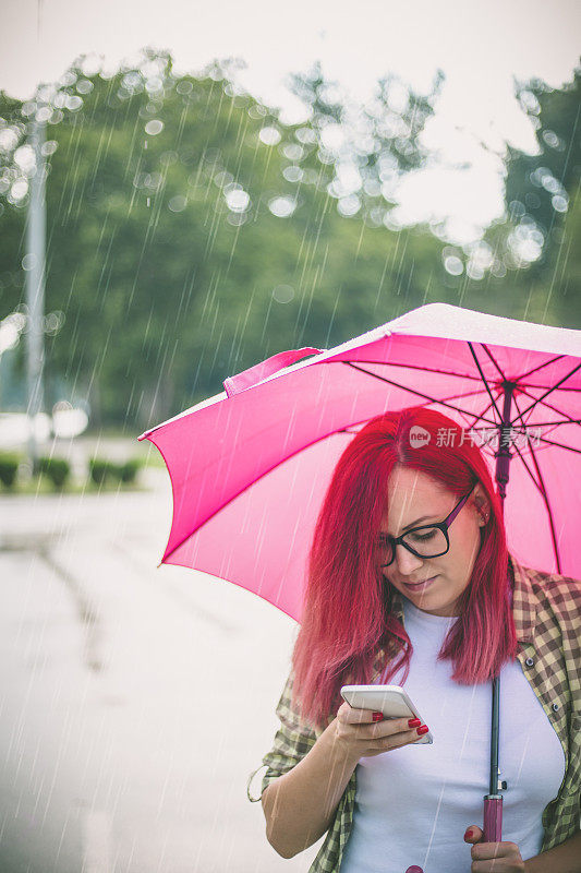 拿着雨伞在街上看手机的女人。