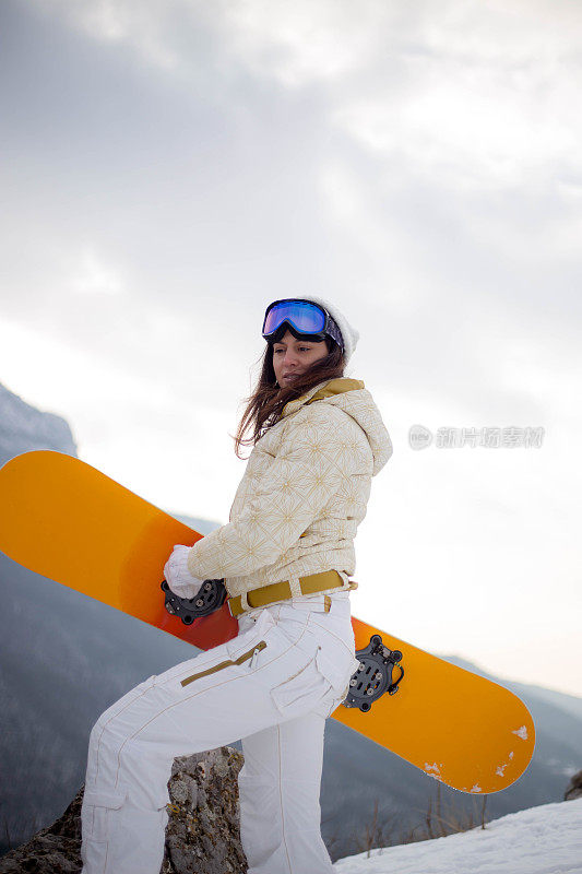 女人拿着滑雪板，背景是高山