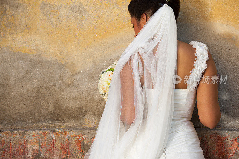 美丽的新娘戴着巨大的面纱站在墙前