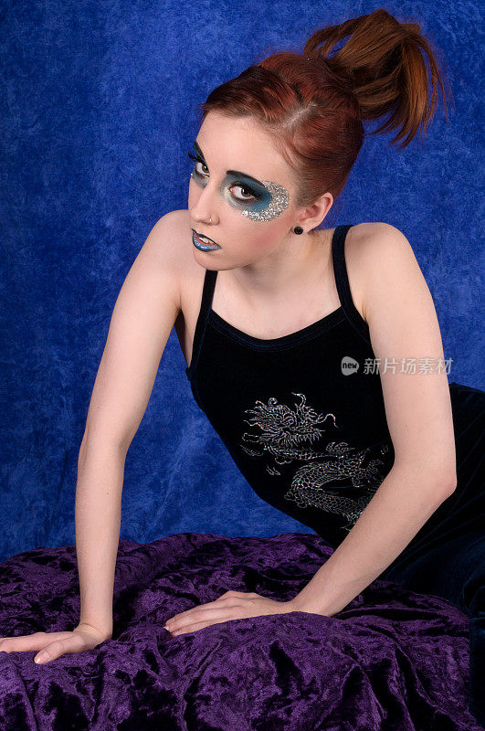涂着蓝眼妆的红发女郎倚靠在紫色天鹅绒上。