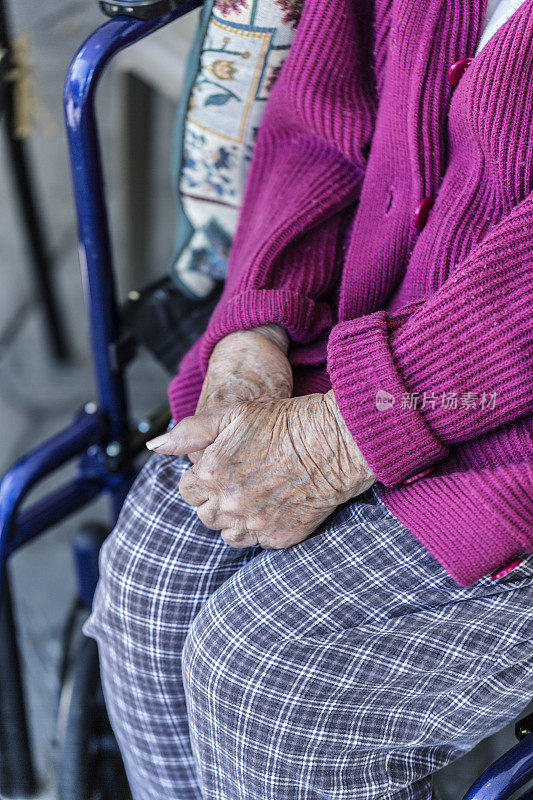 坐在轮椅上双手紧握的老妇人